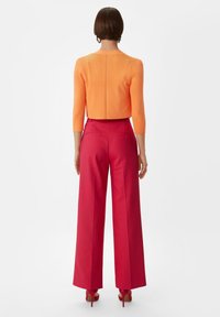 Pomarańczowy krótki sweter z rękawami do trzech kwart, z dopasowanymi jasnoróżowymi spodniami z szerokimi nogawkami o wysokim stanie i pasującymi różowymi szpilkami.