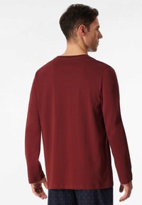 Camisetta a maniche lunghe color marsala con scollatura a girocollo e superficie liscia, mostrata da dietro con un design a vestibilità rilassata.