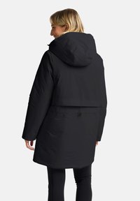 Zwarte, capuchon parka met een hoge kraag, lange mouwen en een getailleerde taille. Glad, waterdicht materiaal met een matte afwerking.