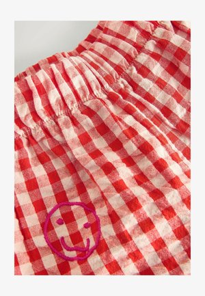 Czerwona i biała tkanina w kratkę z elastycznym pasem; z przodu różowy haftowany uśmiechnięty emblemat.