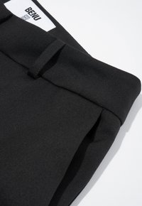Zwarte op maat gemaakte broek met een soepele textuur, voorzien van een schone tailleband en subtiele plooien. Gemarkeerd met een wit label met de tekst "BENU."