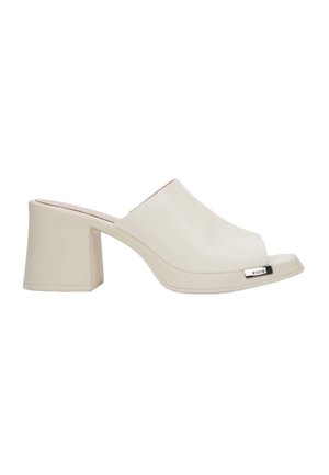 Beige open-toe mule met een glanzende afwerking, blokhak en metallic accent; gladde textuur met een minimalistisch ontwerp.