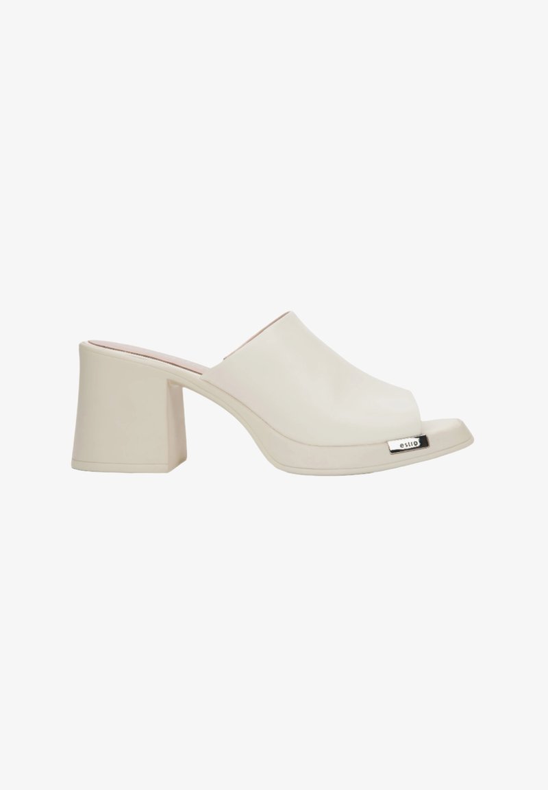 Beige open-toe mule met een glanzende afwerking, blokhak en metallic accent; gladde textuur met een minimalistisch ontwerp.