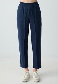 Marineblaue, leichte Hose mit elastischem Bund und geradem Bein. Glatte Textur und dezenter Glanz. Kombiniert mit weißen Sneakers.