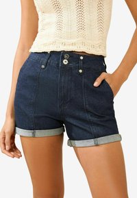 Shorts en denim foncé avec une taille haute, des ourlets retroussés et une fermeture à boutons. Comprend deux poches latérales et des coutures ton sur ton.