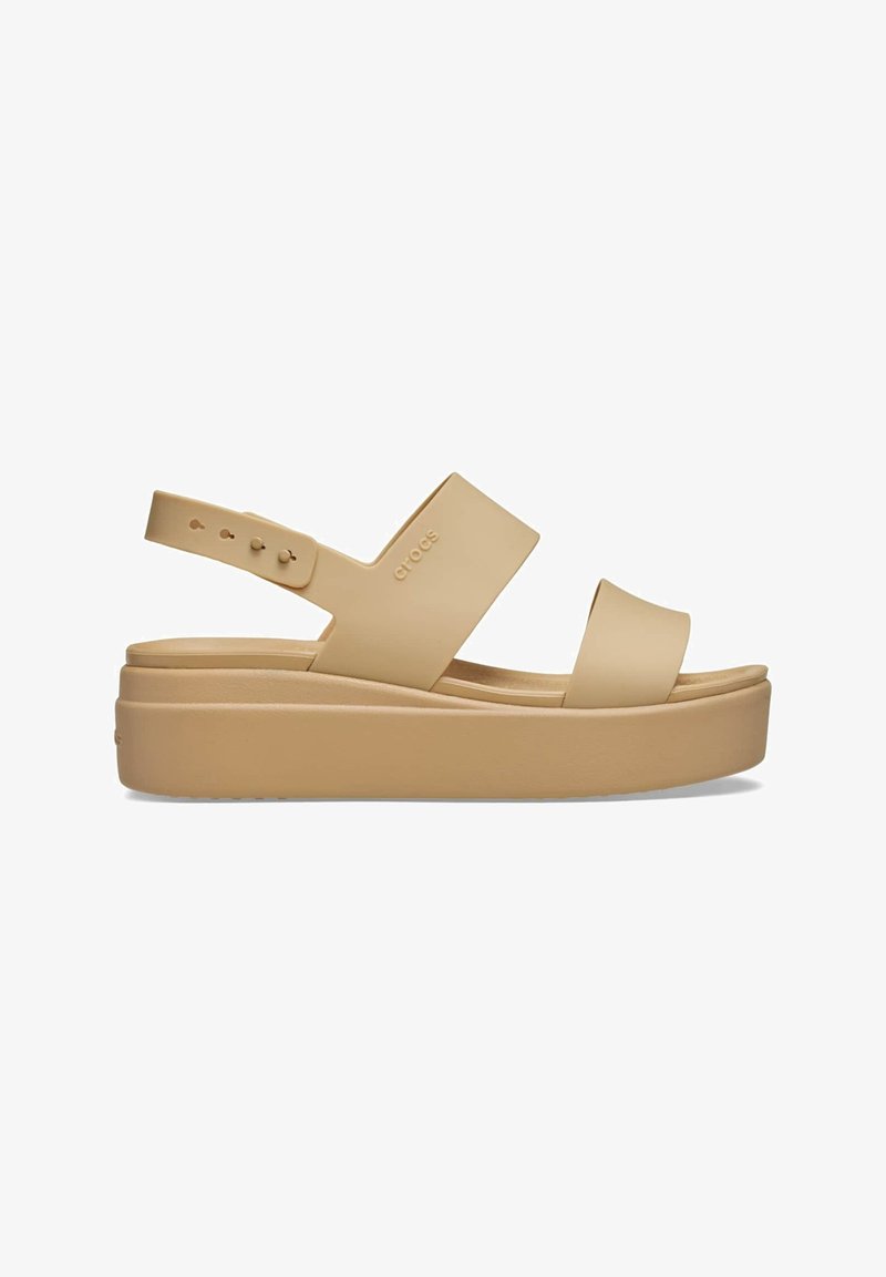 Sandale à plateforme beige avec deux larges brides, bride arrière ajustable et semelle épaisse, marquée d'un logo "crocs" discret sur le côté.