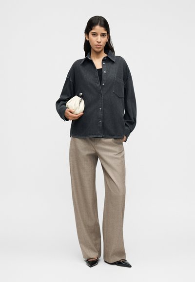 Σκούρο τζιν πουκάμισο με γιακά και κουμπιά μπροστά, σε συνδυασμό με μπεζ παντελόνι με ευρύ μπατζάκι. Λευκό τσαντάκι στο χέρι, μαύρα μυτερά παπούτσια.