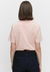 Kortärmad t-shirt med rund hals i ljusrosa, tillverkad av mjukt och slätt tyg; kombinerad med mörka denimjeans med bakfickor.