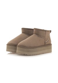 Botas de tobillo de ante marrón con puntera redonda, caracterizadas por una suela gruesa y dentada, y un detalle de costura mínimo en la parte superior.