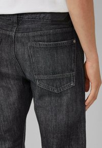 Schwarze Jeans aus Denim mit einer strukturierten Oberfläche. Verfügt über eine Gesäßtasche, sichtbare Nähte und ein kleines Logoschild am Bund.