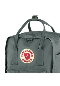 Zaino grigio a forma rettangolare, realizzato in tessuto resistente. Dotato di due manici superiori, chiusura con zip e un pannello rotondo con logo.