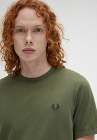 T-shirt a maniche corte di colore verde oliva realizzato in cotone, con una texture morbida e un piccolo logo ricamato nella parte sinistra del petto.