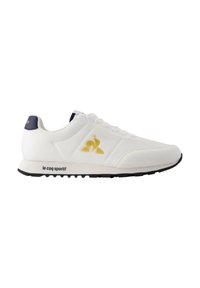 Sneaker atletico bianco con logo giallo e blu scuro, design con lacci, materiale in pelle liscia e suola in gomma nera con battistrada testurizzato.