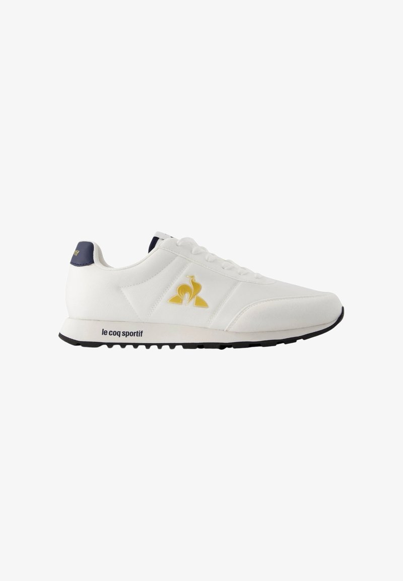 Sneaker atletico bianco con logo giallo e blu scuro, design con lacci, materiale in pelle liscia e suola in gomma nera con battistrada testurizzato.