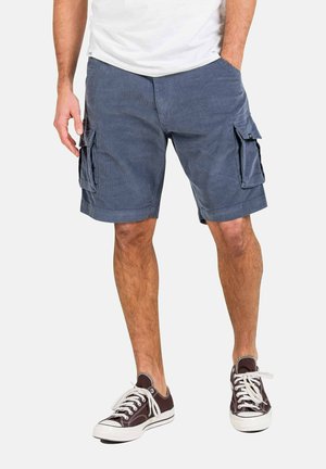 Cargo shorts in dark blue fabric with two large side pockets, flat front, and rolling hem. Paired with brown sneakers and a white t-shirt.