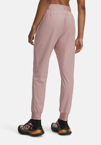 Světle růžové sportovní kalhoty s úzkým střihem, pružným pasem a manžetami u kotníků. Nošeny s tmavými teniskami s barevnými akcenty.