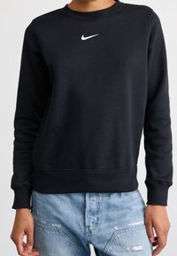 Black sweatshirt with a crew neck and ribbed cuffs, featuring a white Nike logo on the chest. Paired with distressed light blue jeans.