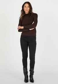 Maglietta marrone a maniche lunghe con scollo texturizzato e arricciato, abbinata a pantaloni neri aderenti e stivali neri al ginocchio. Design semplice e lineare.