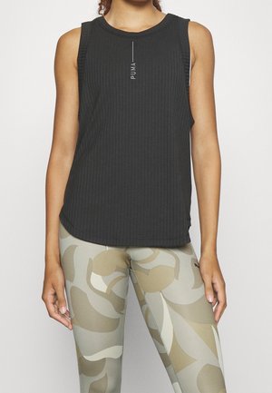 Kvinde iført en sort ærmeløs Puma-top og lyse leggings med store abstrakte bladmønstre.