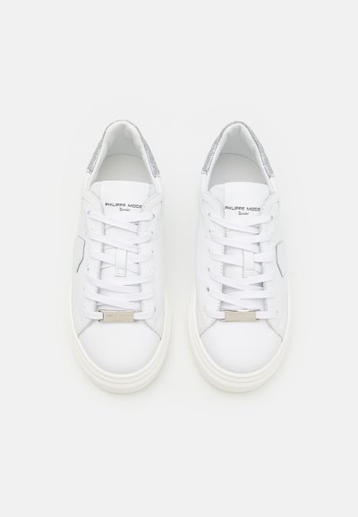 Zapatillas de cuero blanco con acentos de purpurina plateada, cordones planos y una suela de goma texturizada. Presenta detalles de marca en la lengüeta.