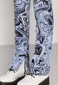 Calças com padrão de mármore azul e preto, em cortes ajustados, combinadas com botas brancas com atacadores, apresentando contornos pretos e fechos laterais visíveis.