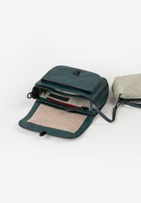 Grüne Lederhandtasche mit Klappe, die ein beiges Wildleder-Innenfutter, Reißverschlusstaschen und eine gestreifte Innenauskleidung zeigt. Enthält einen abnehmbaren Trageriemen.