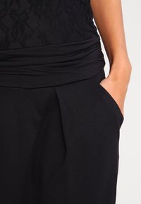 Pantalons noirs ajustés avec un design à plis sur le devant, dotés d'une taille froncée douce et de poches latérales pour plus de fonctionnalité.
