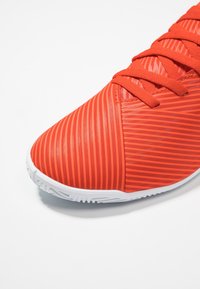 Zapato deportivo rojo con un diseño texturizado que presenta rayas verticales, punta redondeada y suela de goma blanca. Los cordones también son de color rojo brillante.