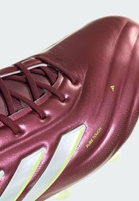 Scarpe da calcio color marrone scuro con una parte superiore lucida e testurizzata, con accenti bianchi e la scritta 'PURE TOUCH' stampata in giallo. I lacci sono di un marrone scuro.