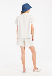 Helles beiges Kurzarm-Polo und Shorts-Set aus strukturiertem Stoff, kombiniert mit einem blauen Bucket Hat mit Belüftungsöffnungen.