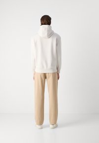 HanORcă albă cu glugă ajustabilă, asortată cu pantaloni bej deschis, cu croială lejeră. Design casual și textură moale, potrivită pentru purtarea de zi cu zi.