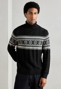 Čierny sveter s rolákom a vrkočovým vzorom, s bielym fair isle vzorom cez hrudník. Mäkká textúra, priliehavý v páse a na manžetách.