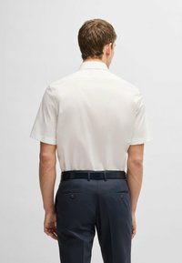 Camicia bianca a maniche corte con una texture liscia. Abbinata a pantaloni a quadri scuri con due tasche posteriori e una cintura nera elegante.