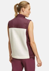 Ärmellose Weste mit einem kastanienbraunen Vorderteil und einem strukturierten weißen Fleece-Rücken, mit glatter Oberfläche und Saumdetails.