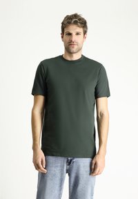 Donkergroene crewneck t-shirt van gladde stof, korte mouwen, aansluitende pasvorm, gecombineerd met lichtblauwe spijkerbroek.