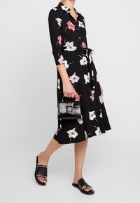 Black floral dress with three-quarter sleeves, button front, and waist tie. Paired with a black croc-embossed handbag and flat black sandals.