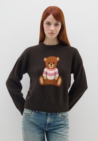 Brauner Pullover mit einem Bärenmotiv. Der Pullover hat einen gerippten Halsausschnitt und einen lockeren Schnitt. Der vordere Bär trägt ein gestreiftes Shirt in Rosa und Weiß.