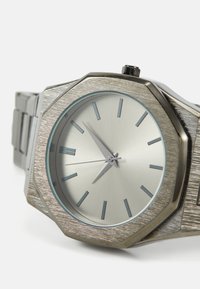 Stainless steel octagonal watch with a brushed silver finish, minimalistic gray dial, and index hour markers. Features a date display.