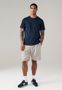 Marineblauwe katoenen t-shirt, grijze shorts, gestructureerde stof, atletische pasvorm. Draagt met marineblauwe sneakers en witte crew-sokken. Eenvoudig, casual ontwerp.