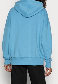Felpa con cappuccio di colore azzurro chiaro, dal taglio rilassato, con polsini e orlo a coste, realizzata in tessuto morbido, con tasca a marsupio e cuciture a vista.