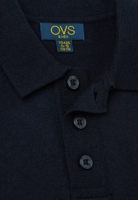 Polo de algodón azul marino con un tejido texturizado, tres botones negros y un cuello. La etiqueta indica talla 4-5 años, CM 110.