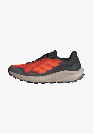 Chaussure de trail pour homme avec un dessus en mesh rouge et des accents noirs, logo GORE-TEX, et une semelle en caoutchouc beige avec une texture antidérapante.