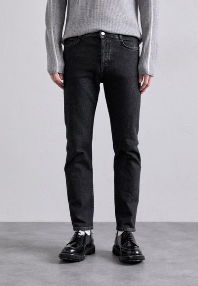 Blugi negri din denim cu o croială slim, cu buzunare frontale, sistem de închidere cu nasture și o textură subtilă. Asortați cu pantofi eleganți negri cu șireturi.