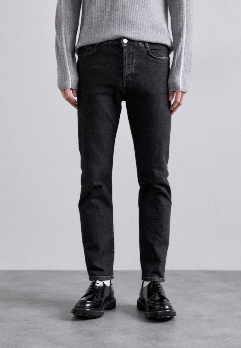 Sorte denim jeans med slim fit, som har frontlommer, knappestang og en subtil tekstur. Kombinert med blanke svarte snørestøvler.