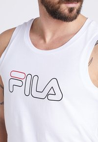 Débardeur en coton blanc arborant un logo Fila noir et rouge bien visible sur la poitrine. Design classique avec des emmanchures larges et un col rond.