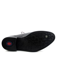 Suela de zapato de cuero negro con un diseño texturizado que presenta varias letras en relieve y un logo circular de color en la zona del talón.