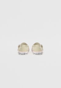 Zapatillas de lona de color verde claro sin cordones, con punta redondeada, que presentan un pequeño lazo decorativo y suelas a rayas en blanco y negro. Marca en el talón.