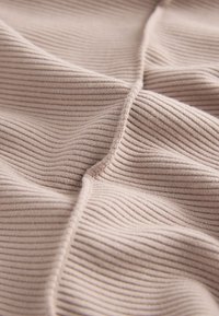 Šviesiai smėlio spalvos ribuotas audinys su lygiu paviršiumi, kuriame tolygiai išsidėsčiusios vertikalios iškilumos ir minkšti raukšlėjimai. Matoma ilgaamžė siūlė.