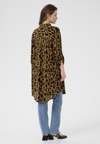 Chemise imprimée léopard avec un ourlet asymétrique, fabriquée dans un tissu léger. Présente des manches trois-quarts et une coupe décontractée. Associée à un jean bleu clair.