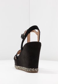 Czarna zamszowa sandał na koturnie z paskiem na kostkę, z plecioną podeszwą w stylu espadrille i gładką wewnętrzną wyściółką.
